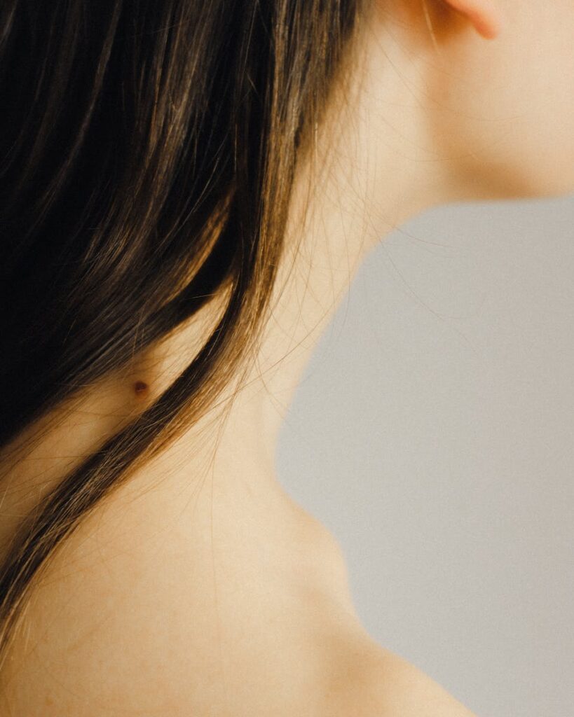 Closeup side view of crop unrecognizable young lady with mole on neck with perfect skin under long dark hair on white background